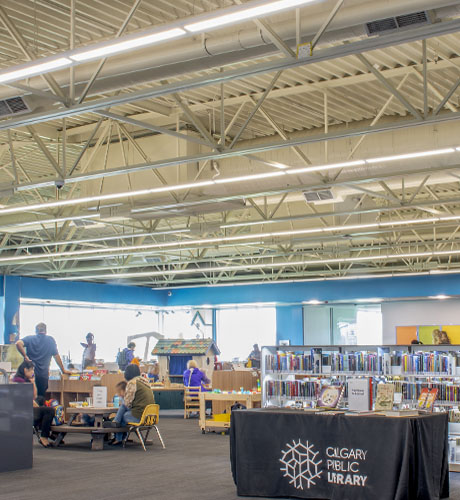 Interior of Calgary Public Library's Crowfoot location. Pictured are tables, bookshelves as well as children playing and reading.