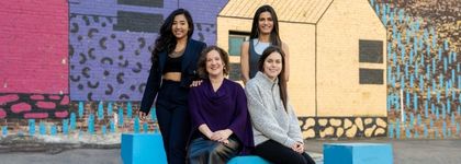 A picture of four women standing and sitting in front of a mural in East Village in Calgary Alberta.