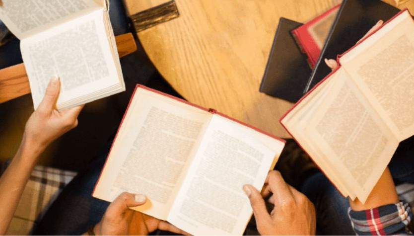 Photograph of three people sitting together at a table with their books open. 