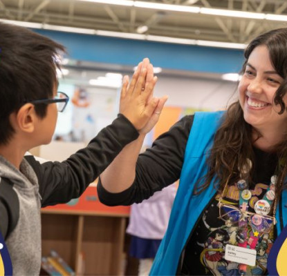 A child and a woman in a blue vest are giving each other a high-five. There is an orange background with red circles illustrations of lightbulbs and books.