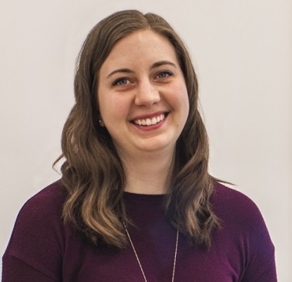 Megan Powell smiling and standing in front of a meeting room with glass doors.