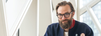 A bearded man with glasses sits in a bright contemporary building.