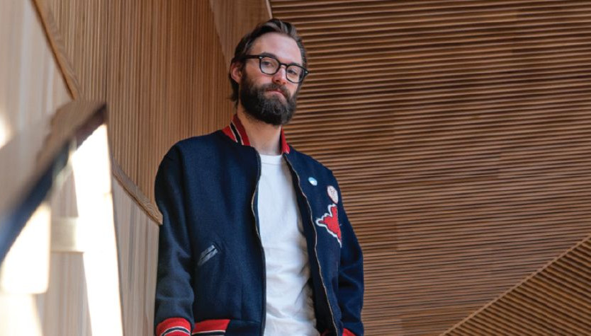 A man with a beard and glasses standing on a staircase in a contemporary building.