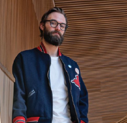 A man with a beard and glasses standing on a staircase in a contemporary building.