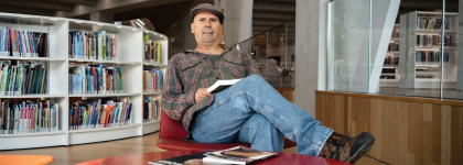 paulo da costa sitting in a chair in a library with a book.