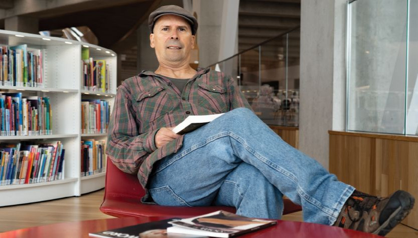 paulo da costa sitting in a chair in a library with a book.