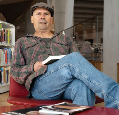 paulo da costa sitting in a chair in a library with a book.