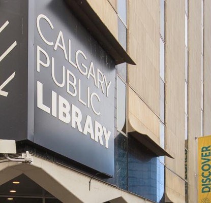 Photograph of the exterior of a building with a large grey sign that reads "Calgary Public Library."