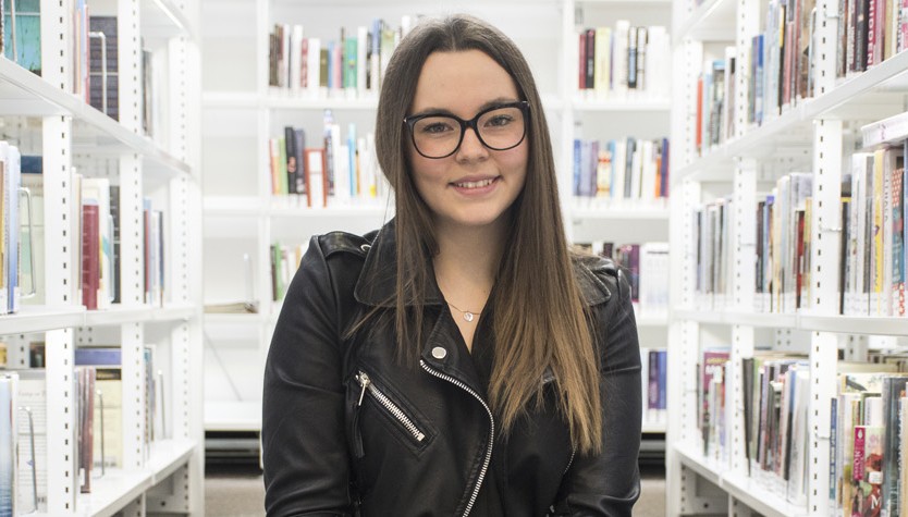 Steph Mok sitting in front of library shelves with books.