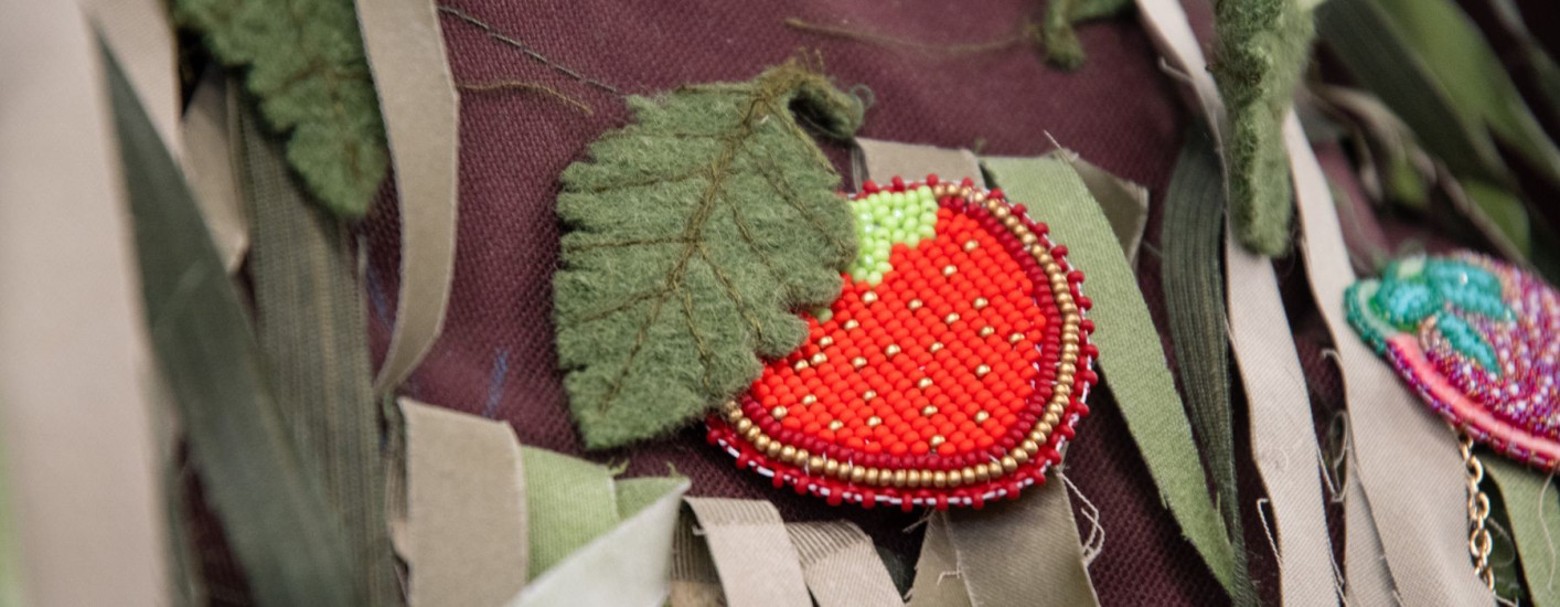 A beaded strawberry on brown cloth with green strips of fabric.