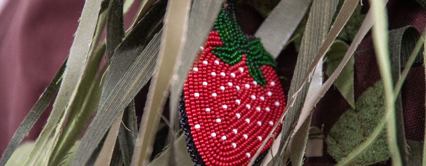 A beaded strawberry on brown cloth with green strips of fabric and cloth leaves.