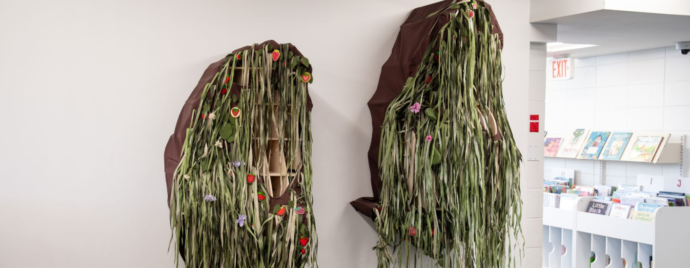 An art installation of beaded strawberries and cloth strips made to look like grass hung on a wall.