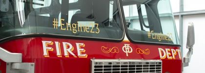 A photograph of the front of a fire truck. Written on the window is #Engine23.