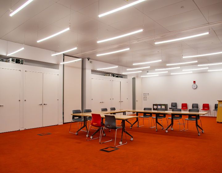 background image: A photograph of a large program room, where the tables are in a "L" shape format with chairs around it.