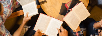 Three adults sitting at a round table reading books.