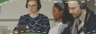 Photo of three people looking at a computer screen and wearing headphones.