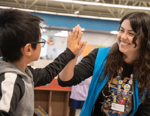 A staff member in a blue vest giving a patron a high five. 