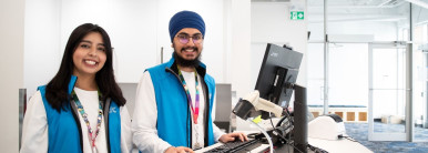 A picture of two Library staff members, a female and a male, standing behind a desk and smiling at the camera.