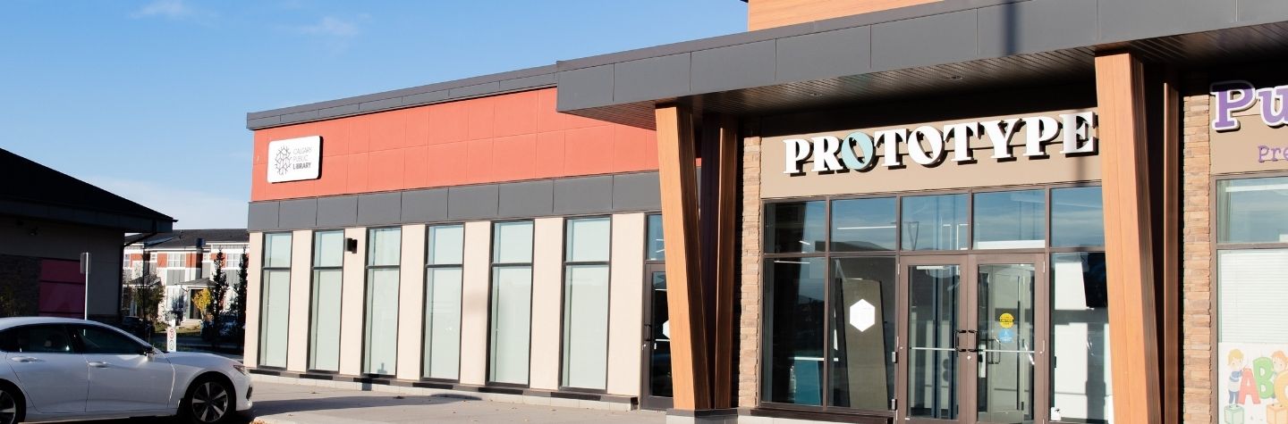 A photo of the front of a brown, red and black building. On top of the door the words Prototype is written in white and blue letters. 